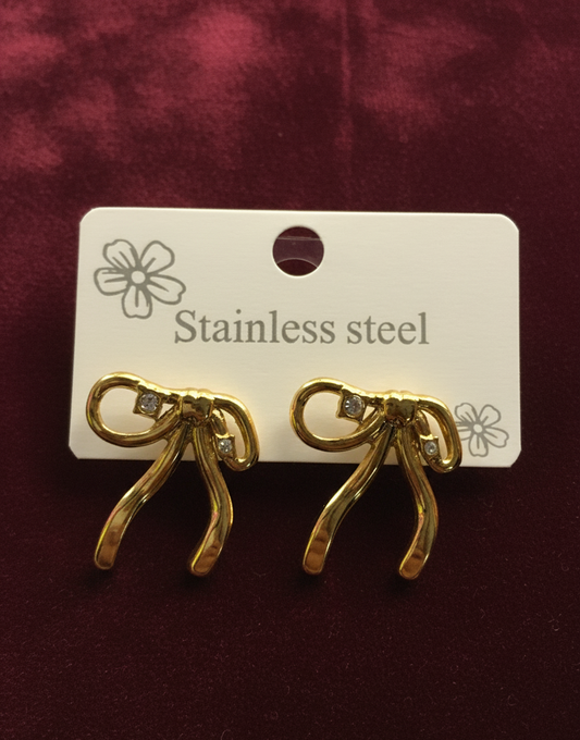 Gold bow-shaped earrings on a white card with 'Stainless steel' text, against a maroon background.