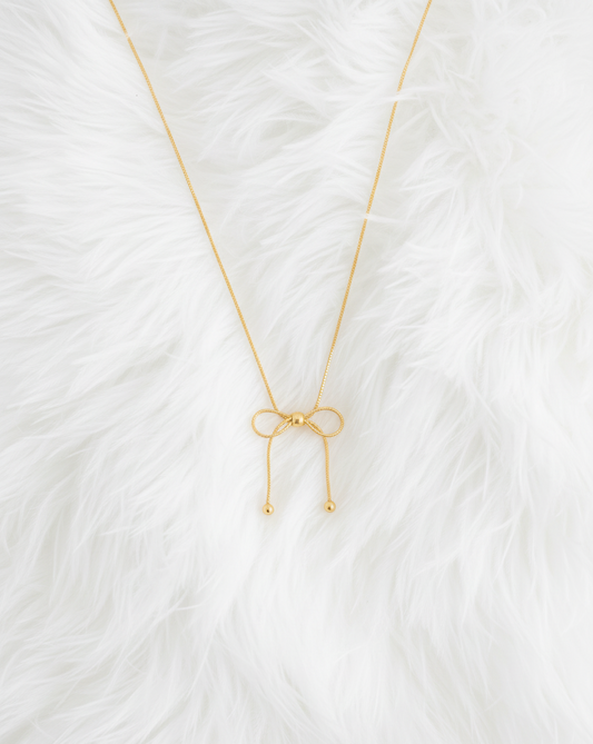 Gold necklace with a bow pendant on a white textured background