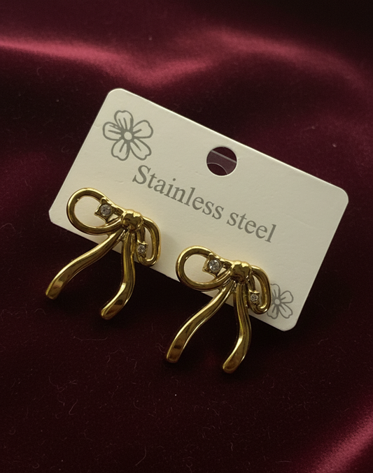 Gold earrings on a white card with 'Stainless steel' text, against a maroon fabric background.