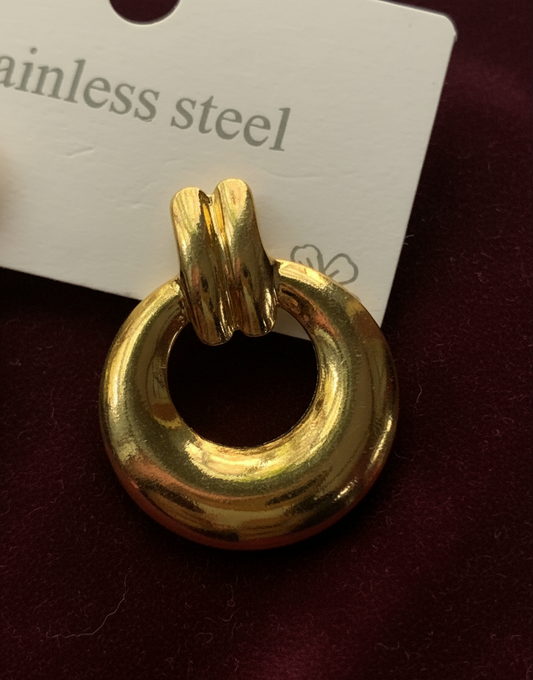 Gold ring pendant on a dark surface with 'stainless steel' text in the background