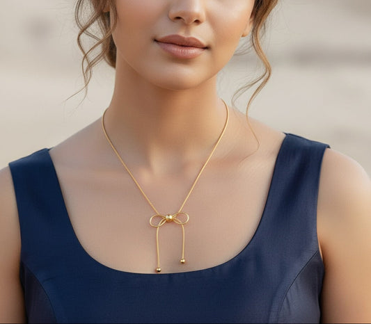 Woman wearing a gold necklace with a bow pendant against a neutral background